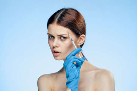 Beautiful young woman on a blue background holds a syringe, medicine, plastic.