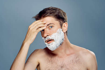 A young guy with a beard on a black background applies a shaving foam.の写真素材