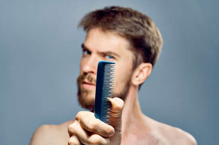 A young guy with a beard on a gray background holds a comb.の写真素材