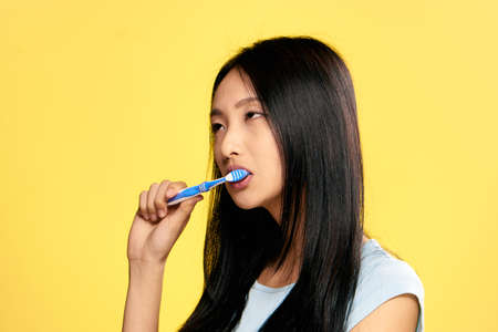 Beautiful young woman on a yellow background brushes teeth, portrait, asian.の写真素材