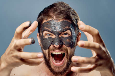 A young guy with a beard on a gray background in a clay facial mask.の写真素材