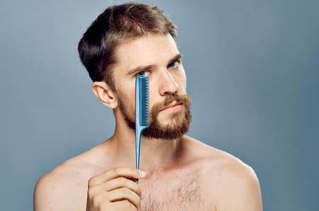A young guy with a beard on a gray background holds a comb.の写真素材