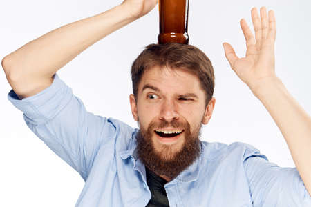 Young guy with a beard on a white isolated background holds a bottle of beer.