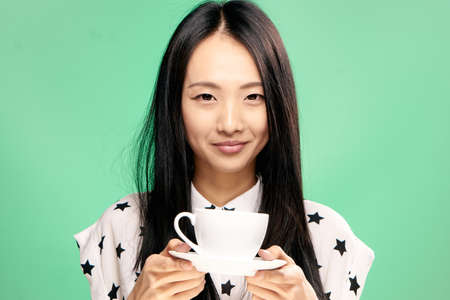 Beautiful young woman on a green background holds a mug, Asian.