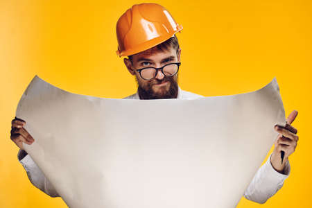 Engineer with a beard on a yellow background holds a drawing.の写真素材