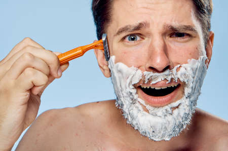 Young guy with a beard on a blue background shaves.の写真素材