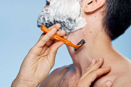 Young guy with a beard on a blue background shaves.の写真素材