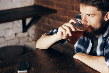 A young guy with a beard drinks beer in a bar.