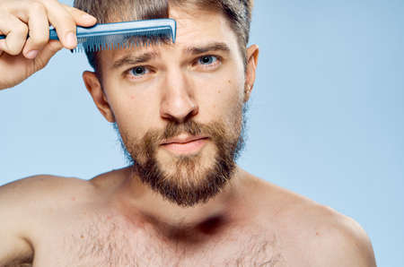 Young guy with a beard on a light background holds a comb.の写真素材