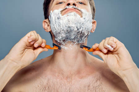 Young guy with a beard on a gray background shaves.