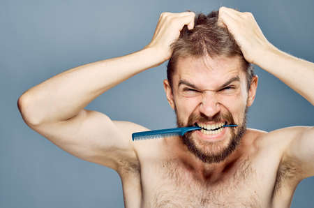 A young guy with a beard on a gray background holds a comb.の写真素材