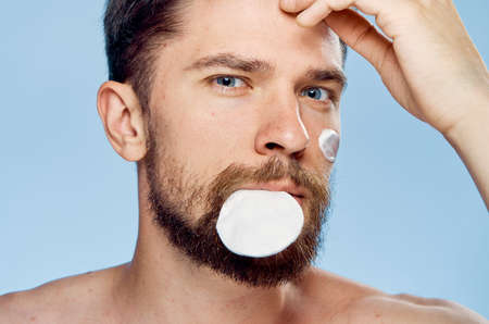 A young guy with a beard with a blue background, a cotton ball, a cosmetic cream.の写真素材
