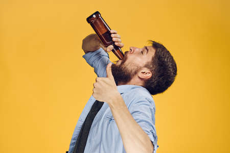 Young guy with a beard with on a yellow background holds a bottle of beer.の写真素材