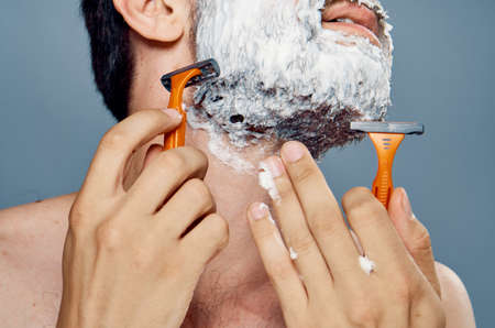 Young guy with a beard on a gray background shaves.の写真素材