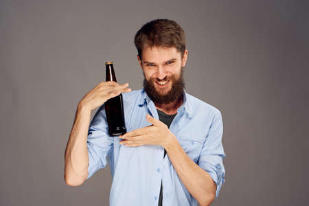 A young guy with a beard on a gray background holds a bottle of beer.の写真素材