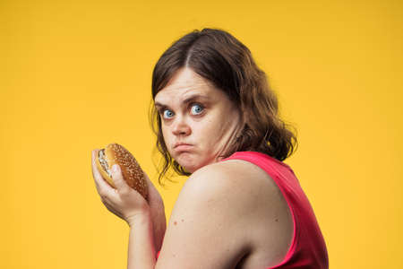Fat woman on a yellow background holds a hamburger.の写真素材