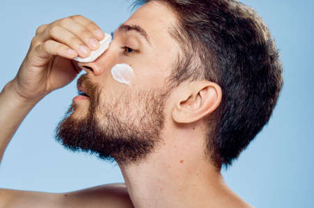 Young guy with a beard on a blue background, cream, cotton ball.の写真素材