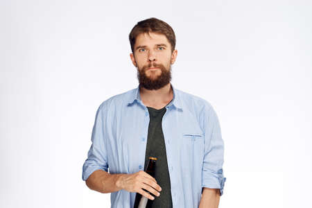 Young guy with a beard on a white isolated background holds a bottle of beer.