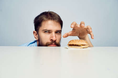 Young guy with a beard on a light background at a table next to a hamburger.の写真素材