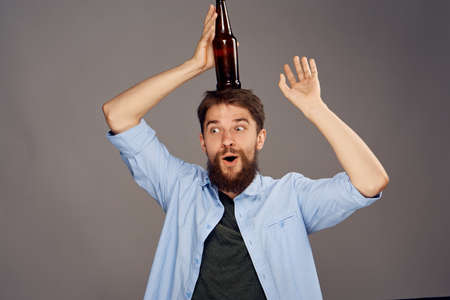 A young guy with a beard on a gray background holds a bottle of beer.の写真素材