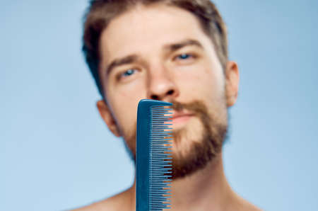 Young guy with a beard on a blue background holds a comb.の写真素材
