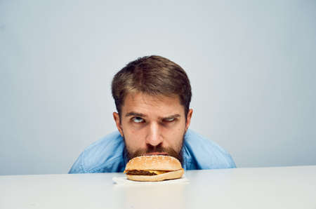 Young guy with a beard on a white isolated background looks at a hamburger.