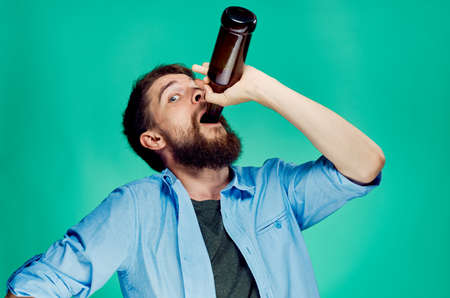 A young guy with a beard on a green background holds a bottle of beer.の写真素材