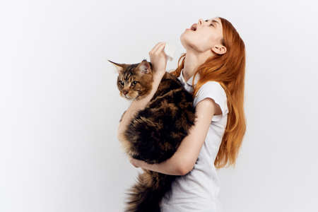Beautiful young woman on white isolated background holds a cat, an allergy.の写真素材