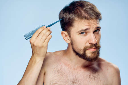 Young guy with a beard on a blue background holds a comb.の写真素材