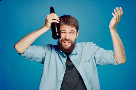 A young guy with a beard on a blue background holds a bottle of beer.の写真素材