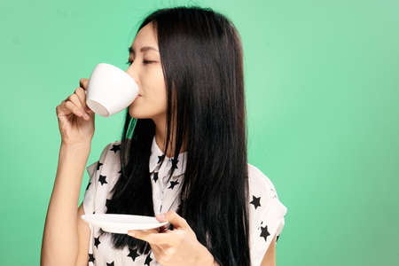 Beautiful young woman on a green background holds a mug, Asian.の写真素材