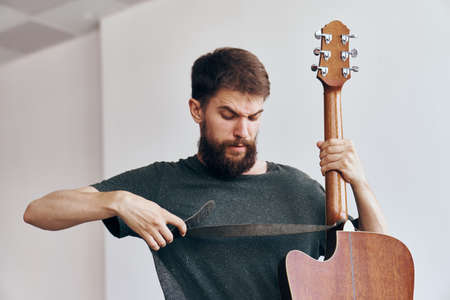 Young guy with a beard on a white isolated background holds a guitar.