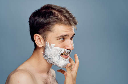 Young guy with a beard on a gray background in shaving foam.の写真素材