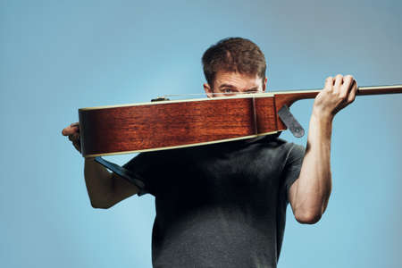 Young guy with a beard on a blue background holds a guitar.