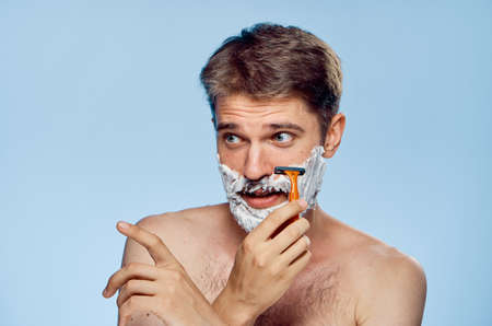 Young guy with a beard on a blue background shaves.の写真素材