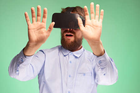 A young guy with a beard on a green background with virtual reality glasses.の写真素材