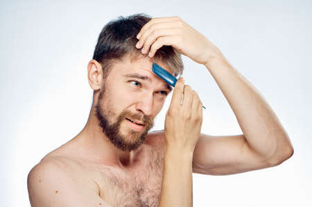 Young guy with a beard on a light background combs his hair.の写真素材