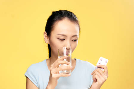 Beautiful young woman on a yellow background holds a pill, medicine, asian.