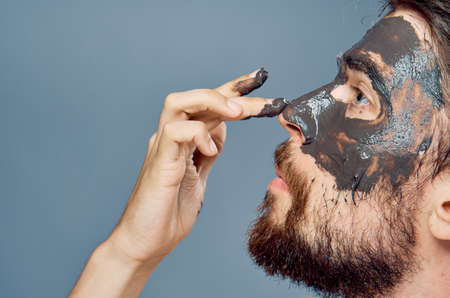 A young guy with a beard on a gray background applies clay cosmetic face mask.の写真素材