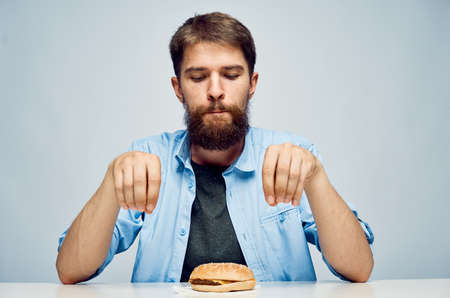 Young guy with a beard on a light background looks at a hamburger.の写真素材