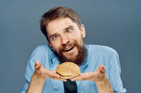 Young guy with a beard on a gray background holds a hamburger.