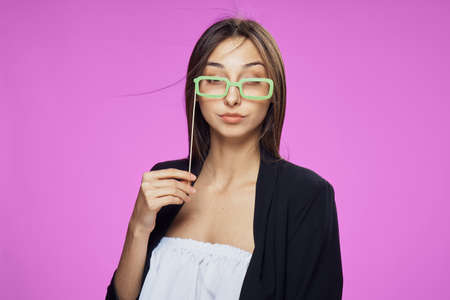 Young beautiful woman on a pink background holds paper accessories for parties and holidays.