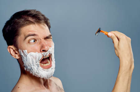 A man with a beard on a gray background in shaving foam holds a razor.の写真素材
