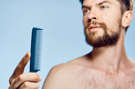 Man with a beard on a blue background holds a comb.の写真素材