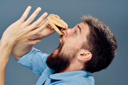 Man with a beard on a black background holds a hamburger, fast food.の写真素材