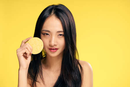 Beautiful young woman on a yellow background holds a sponge for make-up removal, asian.の写真素材