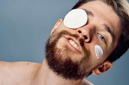 Man with a beard on a gray background, cosmetic cream, cotton pads.の写真素材
