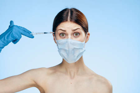 Beautiful young woman on a blue background holds a syringe, medicine, plastic surgery.の写真素材