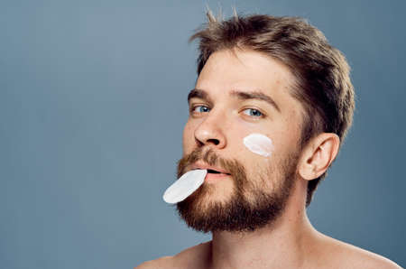 Man with a beard on a gray background, cosmetic cream, cotton pads.
