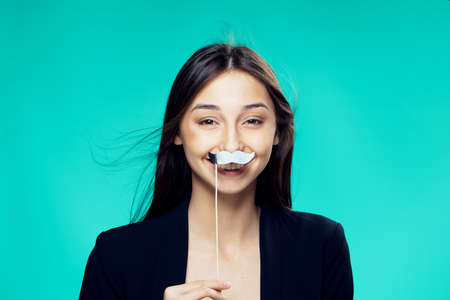 Beautiful young woman on a green background holds paper accessories for parties.の写真素材